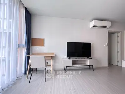 Modern living room with sleek TV setup and stylish desk, featuring natural light from large windows.