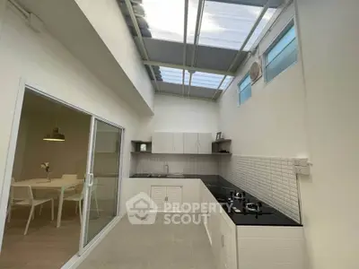 Modern kitchen with open layout and skylight, featuring sleek countertops and dining area.