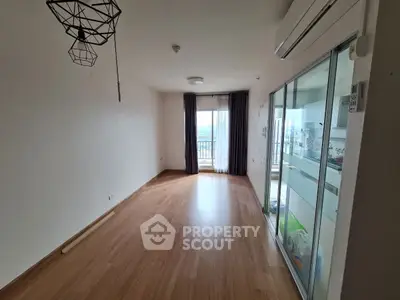 Spacious empty living room with wooden flooring and balcony view.