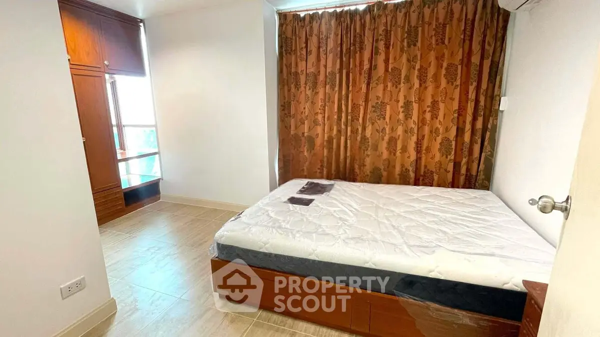 Cozy bedroom with wooden wardrobe and large window, perfect for relaxation.