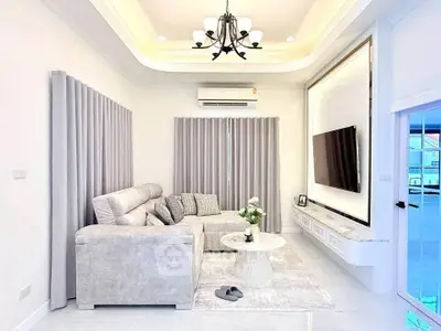 Elegant living room with modern decor, featuring a plush sectional sofa, stylish chandelier, and wall-mounted TV.