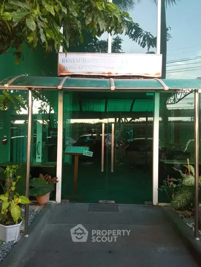 Modern building entrance with glass doors and lush greenery, perfect for commercial real estate.