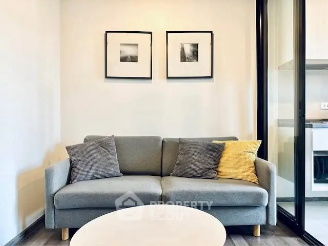 Modern living room with stylish sofa and framed art, adjacent to sleek kitchen area.