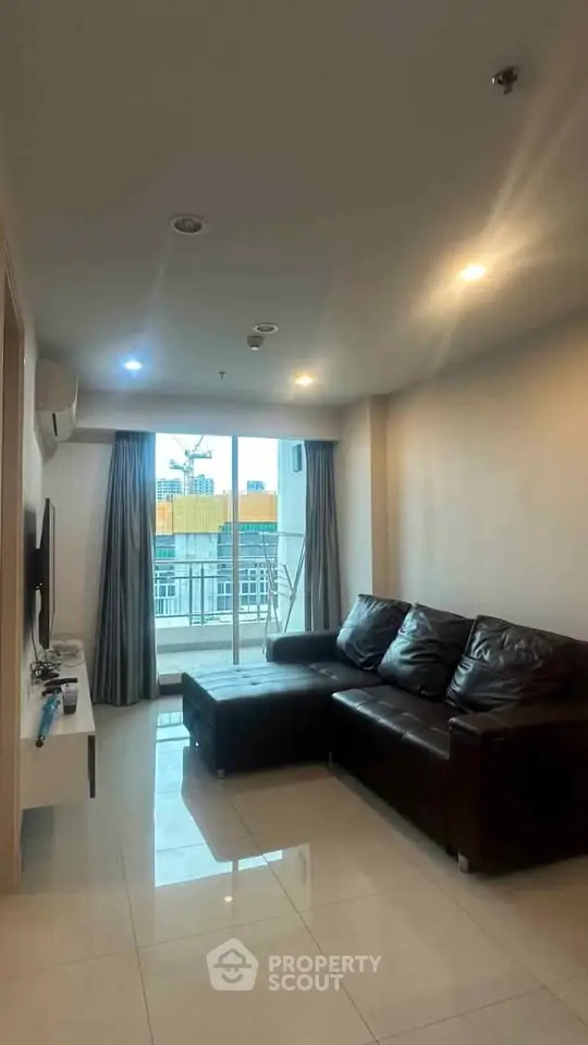 Modern living room with leather sofa and city view balcony in high-rise apartment.