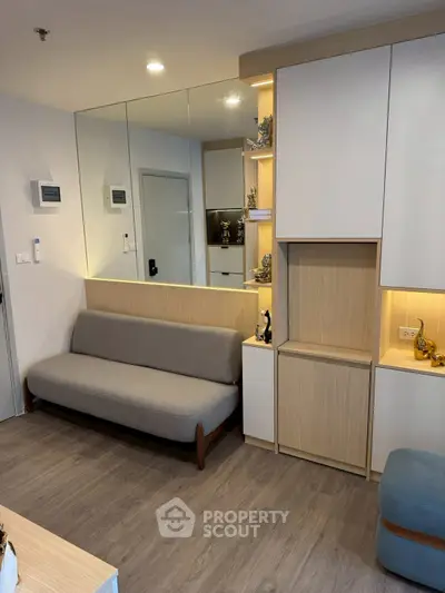 Modern living room with sleek furniture and built-in storage, featuring a stylish mirror wall and cozy ambiance.