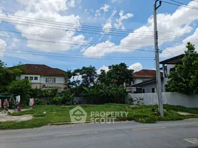 Vacant land plot in suburban neighborhood with clear skies and residential houses nearby.