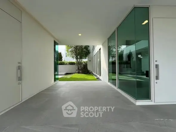 Modern building entrance with sleek glass doors and lush green garden view.