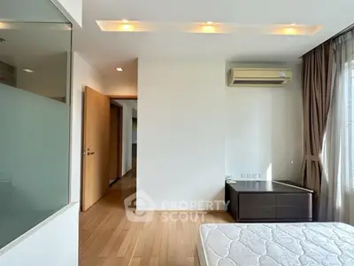 Spacious bedroom with wooden flooring and natural light, featuring air conditioning and modern design.