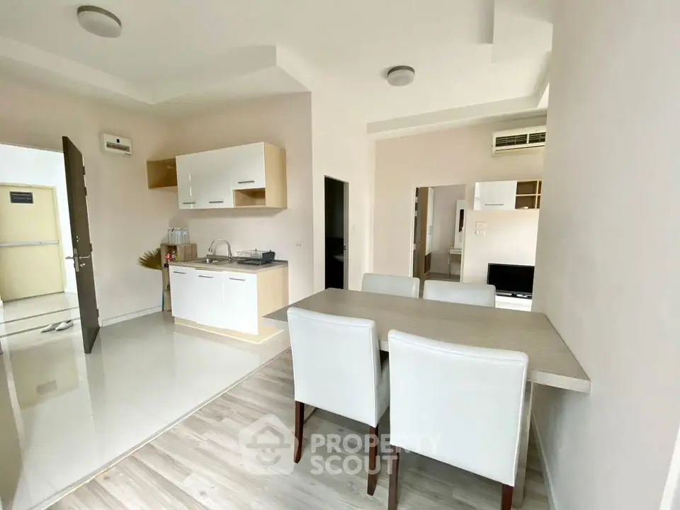 Modern open-plan kitchen and dining area with sleek white furniture and wood accents.