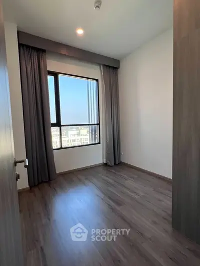 Spacious empty room with large window and wooden flooring, perfect for customization.