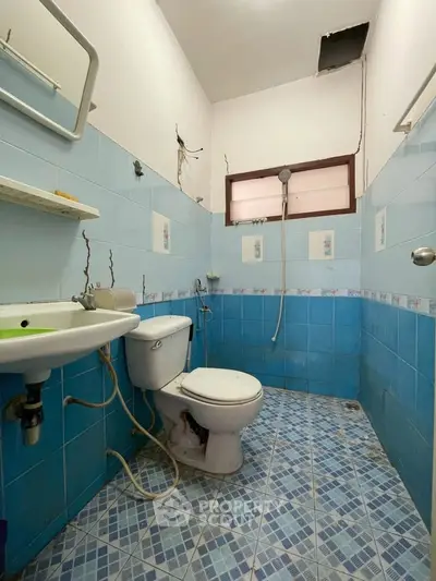 Compact bathroom with blue tiles and basic fixtures, featuring a shower and toilet in a simple layout.