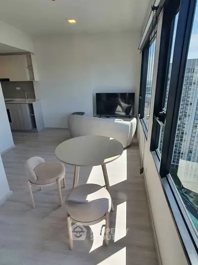 Modern living room with large windows and city view, featuring sleek furniture and open kitchen layout.