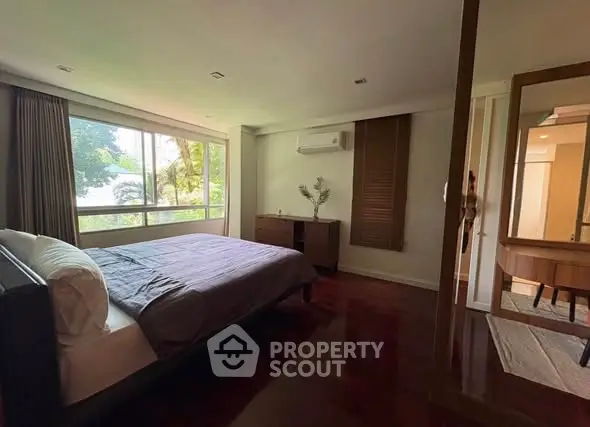 Spacious bedroom with large window and modern furnishings, offering serene garden views.