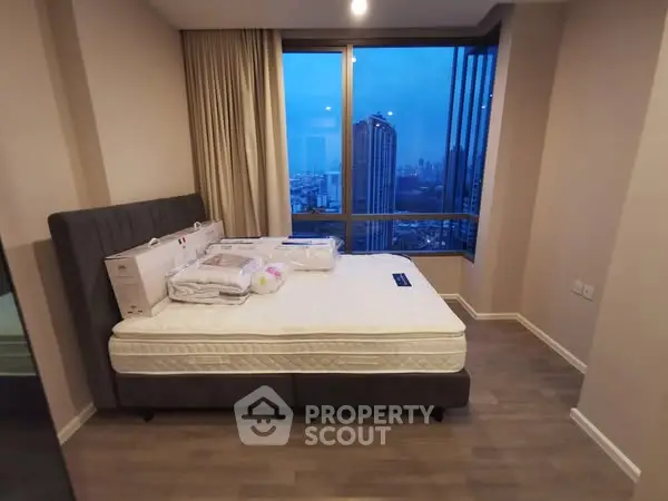 Modern bedroom with city view and large window, featuring a comfortable bed and stylish decor.
