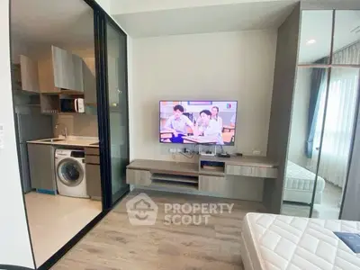 Modern studio apartment with open kitchen and washing machine, featuring a cozy living area with TV.