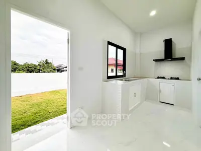 Modern kitchen with open layout and garden view, featuring sleek white design and gas stove.