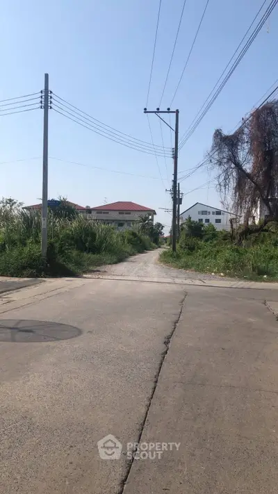 Scenic suburban street view with lush greenery and distant houses under clear blue sky.