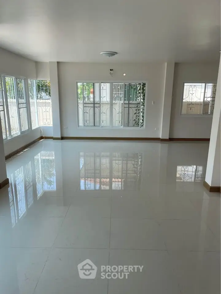Spacious and sunlit living room with gleaming tiled floors, large windows with protective grills, and ample natural light, perfect for family gatherings and entertaining guests.