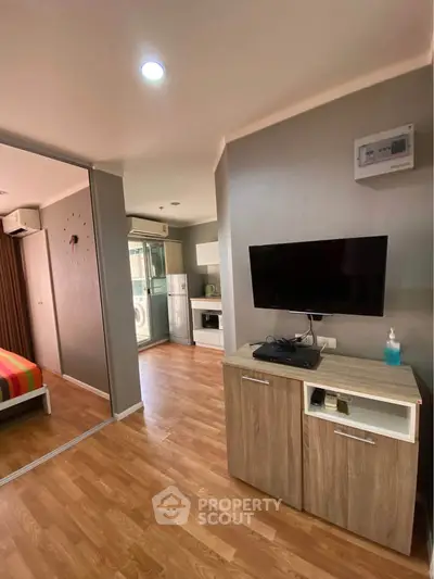 Modern living room with wooden flooring and TV unit, adjacent to a cozy bedroom.