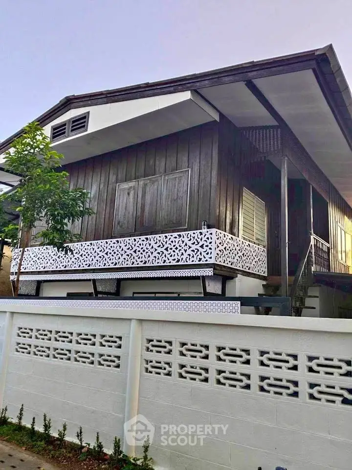 Charming traditional wooden house with intricate balcony design and lush greenery.