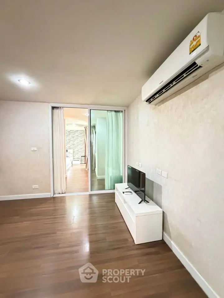 Modern living room with wooden flooring and air conditioning, featuring a sleek TV stand and sliding glass doors.