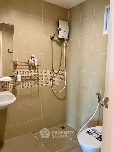 Modern bathroom with shower, sink, and toilet in a tiled setting.