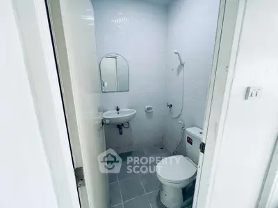 Compact bathroom with white tiles, shower, sink, and toilet in a minimalist design.
