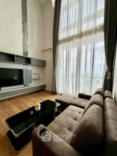 Luxurious living room with high ceilings, large windows, and modern furniture offering stunning city views.