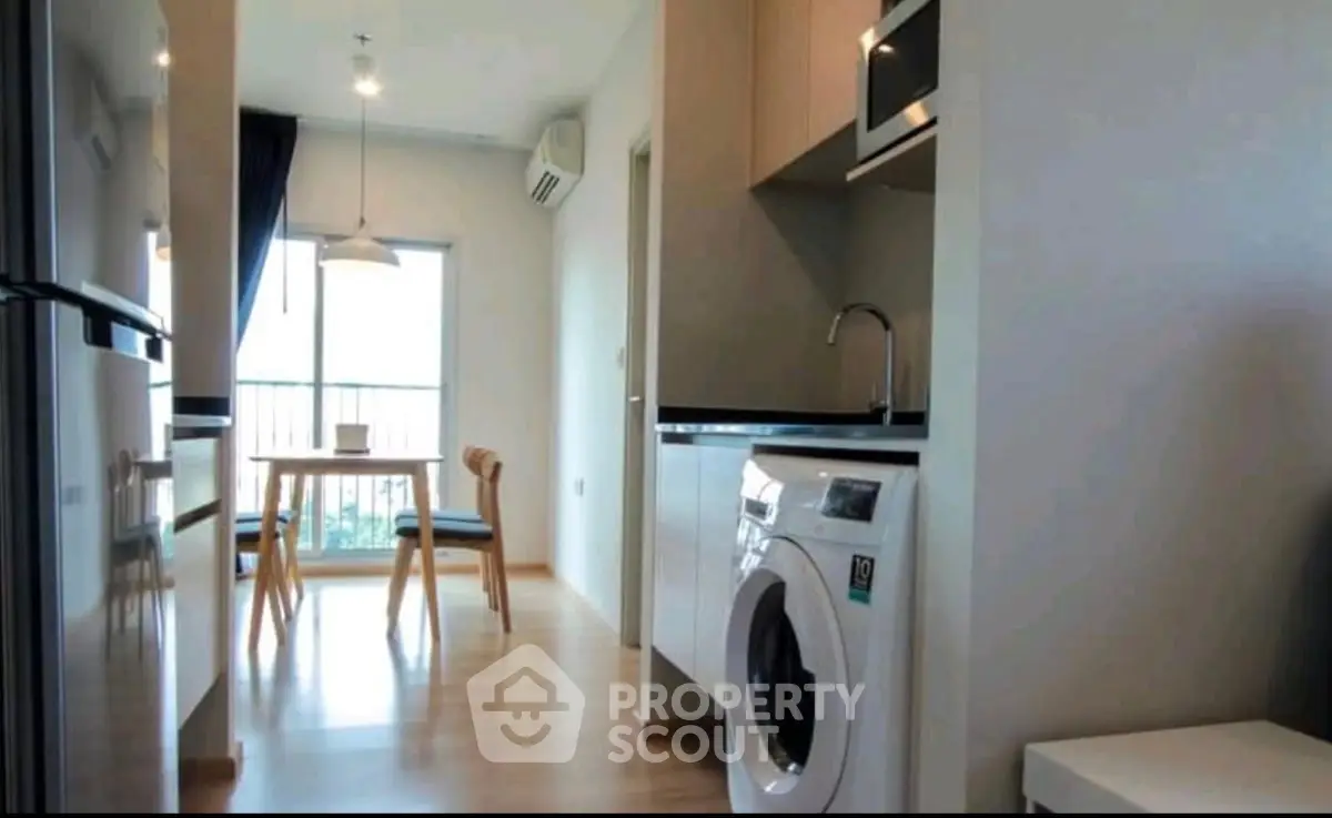 Modern apartment kitchen with washing machine and dining area, featuring sleek design and natural light.