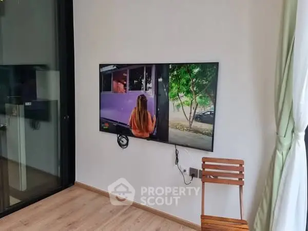 Modern living room with wall-mounted TV and wooden chair, featuring sleek glass partition.
