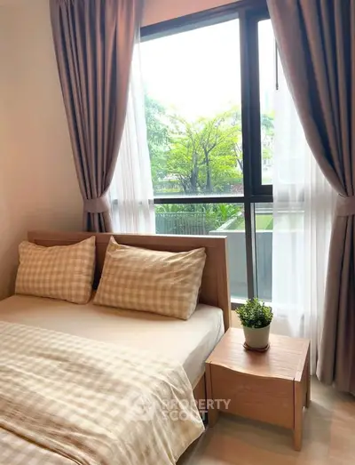 Cozy bedroom with large window and garden view, featuring stylish bedding and wooden furniture.