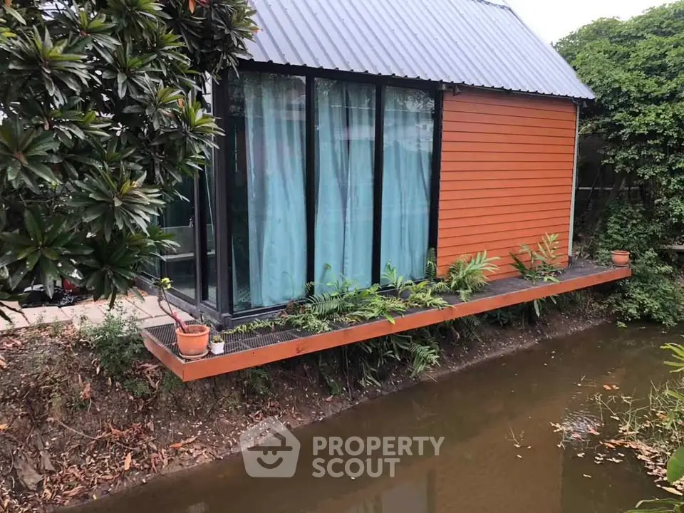 Charming small house with modern design by a tranquil waterway, surrounded by lush greenery.
