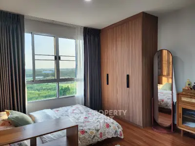 Cozy bedroom with large window and wooden wardrobe, offering serene views and natural light.