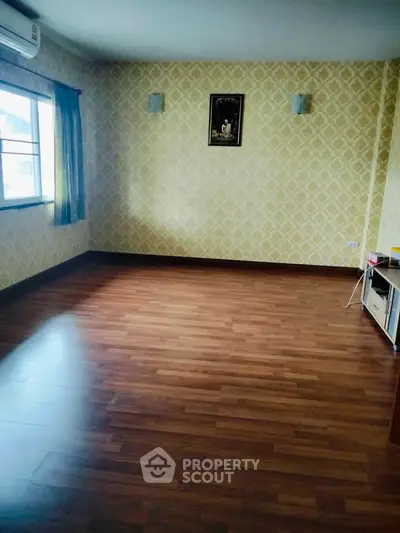 Spacious empty room with wooden flooring and patterned wallpaper, ideal for customization.