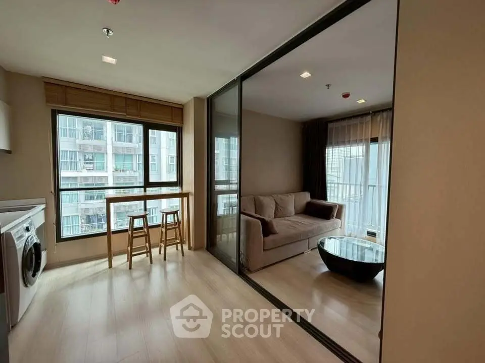 Modern living room with glass partition and washing machine, featuring a cozy sofa and natural light.