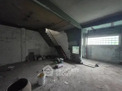 Spacious industrial-style room with concrete floors and staircase, ideal for renovation.