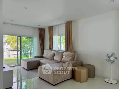 Spacious living room with plush sofa and large windows overlooking greenery.