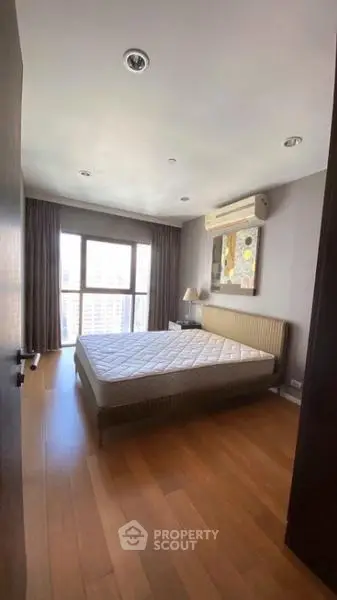 Spacious bedroom with large window and wooden flooring in modern apartment