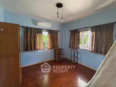 Spacious bedroom with wooden flooring and natural light in a serene setting.