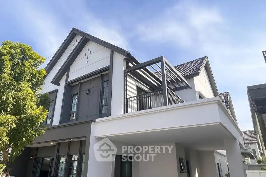 Modern two-story house with sleek design and spacious balcony under clear blue sky.