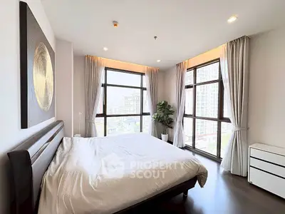 Spacious bedroom with large windows offering stunning city views, modern decor, and ample natural light.