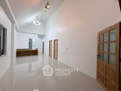 Spacious modern interior with high ceilings and elegant lighting, featuring a wooden door and sleek tiled flooring.