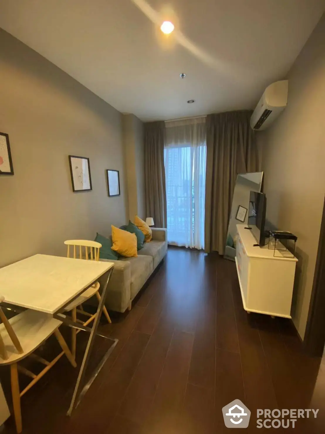 Cozy and inviting living room with comfortable seating, modern dining set, and warm wooden flooring, leading to a sunlit balcony.