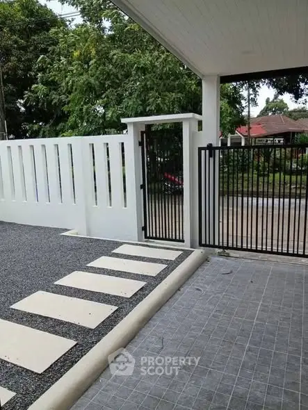 Modern residential entrance with sleek gate and pathway, surrounded by lush greenery.