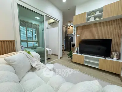 Modern living room with cozy sofa, TV unit, and view into bedroom through glass doors.