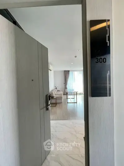 Modern apartment entrance with open door revealing stylish living room and natural light.