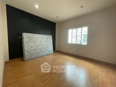 Spacious empty bedroom with wooden flooring and large window, ready for customization.