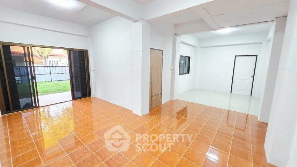 Spacious open-plan living area with glossy tile flooring and sliding glass doors leading to a garden view.