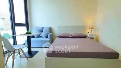 Modern bedroom with large window, cozy seating area, and stylish decor in a high-rise apartment.