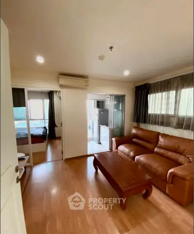 Cozy living room with leather sofa and wooden floor, connecting to bedroom and laundry area.